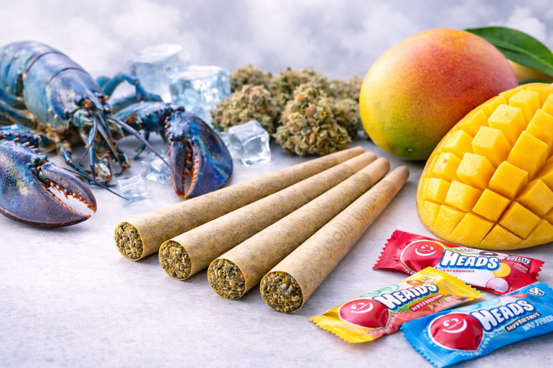 Four cone-style prerolls arranged on a surface alongside a blue lobster, fresh mango slices, cannabis flower, and colorful candy, representing different strain inspirations.